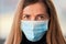 Young woman wearing blue disposable mouth face nose virus mask, closeup portrait, focus on her eyes - can be used during