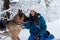 Young woman, wearing blue ski suit, playing with two german shepherds in snow in park. Female master training her dogs in forest