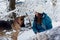 Young woman, wearing blue ski suit, playing with two german shepherds in snow in park. Female master training her dogs in forest