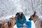 Young woman, wearing blue ski suit, playing with two german shepherds in snow in park. Female master training her dogs in forest