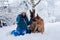 Young woman, wearing blue ski suit, sitting with two german shepherds in snow in park. Female master training her dogs in forest