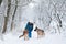 Young woman, wearing blue ski suit,walking with two german shepherds in snow in park. Female master training her dogs in forest