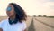 Young woman wearing blue sunglasses walking in a field listening to music on wireless headphones