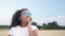 Young woman wearing blue sunglasses walking in a field listening to music on wireless headphones