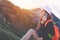 Young woman wearing a hat and backpack talking on the smartphone, sitting high in beautiful mountain reserve at sunset