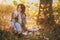 Young woman wearing knitted poncho having picnic in a forest: drinking tea and picking apples