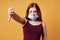 Young woman wearing medical face mask wrong under nose and making thumbs down gesture