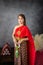 young woman wearing a original traditional red Thai dress and golden ornaments stands holding a jasmine garland. Thai national