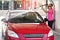 Young woman wearing pink t shirt and sunglasses cleaning her car in self service carwash, spraying water over front windshield and