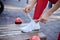 Young woman, wearing red fitness outfit, tying shoe laces on white sneakers. Process of fastening sport shoes. Close-up shot of