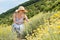 Young woman wearing striped summer dress and straw hat squating in super bloom of wildflowers, relaxing while picking