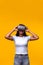 Young woman wearing VR headset on yellow background. Vertical portrait of Asian female wearing virtual reality goggles.