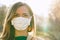 Young woman wearing white cotton virus mouth nose mask, nice backlight sun bokeh in background, closeup face portrait