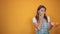 Young woman wearing white t-shirt, over orange background shows emotions