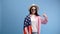 Young woman wears casual clothes and white hat holding american flag and shows a finger up gesture