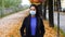 Young woman wears surgical mask in the time of the Covid-19 pandemic. Autumn scenery with trees and falling leaves