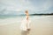 Young woman in wedding dress goes over sea turning back. bride on the beach.