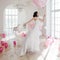 Young woman in wedding dress in luxury interior flies on pink and white balloons.