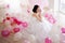 Young woman in wedding dress in luxury interior with a mass of pink and white balloons.