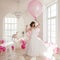 Young woman in wedding dress in luxury interior with a mass of pink and white balloons.