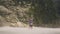 Young woman in wet clothes enjoying flowing waterfall in tropical forest. Happy woman standing under splashing water