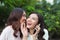 Young woman whispering into cheerful friend`s ear while on call