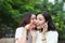 Young woman whispering into cheerful friend`s ear while on call