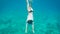 Young woman in white chemise and black swimsuit diving into the ocean to reach the bottom. Female diver swimming and