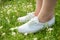 Young woman in white classic sneakers standing in grass on spring meadow