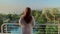 Young woman in a white coat opening curtains and enjoying sea view from terrace in morning.