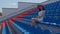 Young woman in in white dress and elegant hat looks away, sitting on stadium bleachers alone. Lonely spectator at street