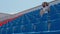 Young woman in in white dress and elegant hat looks away, sitting on stadium bleachers alone. Lonely spectator at street