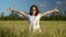 A young woman in a white dress jumps out of a green wheat field. The girl suddenly appears and smiles.