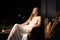 A young woman in a white dress sits thoughtfully in an armchair in a dark room. Solitude, introspection concept