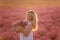 Young woman in white dress stands with handmade basket in hands in purple lavender in field. Allergy