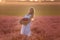 Young woman in white dress stands with handmade basket in hands in purple lavender in field. Allergy