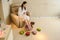 young woman in a white robe sitting in a armchair and relaxing her feet in a silver spa bowl with water surrounded by flowers