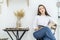 A young woman in a white shirt and jeans sits in a cafe at a table with a tablet in her hands. Female office worker at