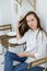 A young woman in a white shirt and jeans sits in a cafe at a table with a tablet in her hands. Female office worker at