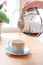 Young woman in white shirt pours morning coffee into cup