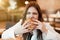 Young woman in white stylish blouse biting with appetite fresh tasty burger during lunch in trendy cafe feeling ultimate hunger