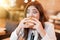 Young woman in white stylish blouse biting with appetite fresh tasty meat burger during lunch in trendy cafe looking very hungry