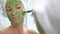 A young woman with a white towel put on her face a green moisturizing mask