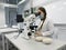 A young woman in a white uniform is working in a laboratory behind a microscope .