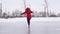 Young woman in winter clothes and high-heeled shoes glides on ice. Crazy female on outdoor ice rink in winter time.