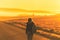 Young woman in the winter jacket with a backpack on the road against the background of the sunrise autumn field.