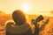 Young woman in the winter jacket with camera on the road against the background of the sunrise autumn field.