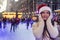 A young woman in winter knit clothes and a santa hat enjoys an ice rink and christmas market in London