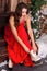 A young woman in winter red dress on a porch decorated with Christmas decorations , putting on skates looking down