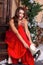 A young woman in winter red dress on a porch decorated with Christmas decorations , putting on skates and smiling.